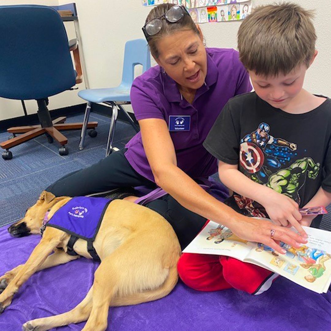 young teenager reading a book with woman volunteer and therapy dog