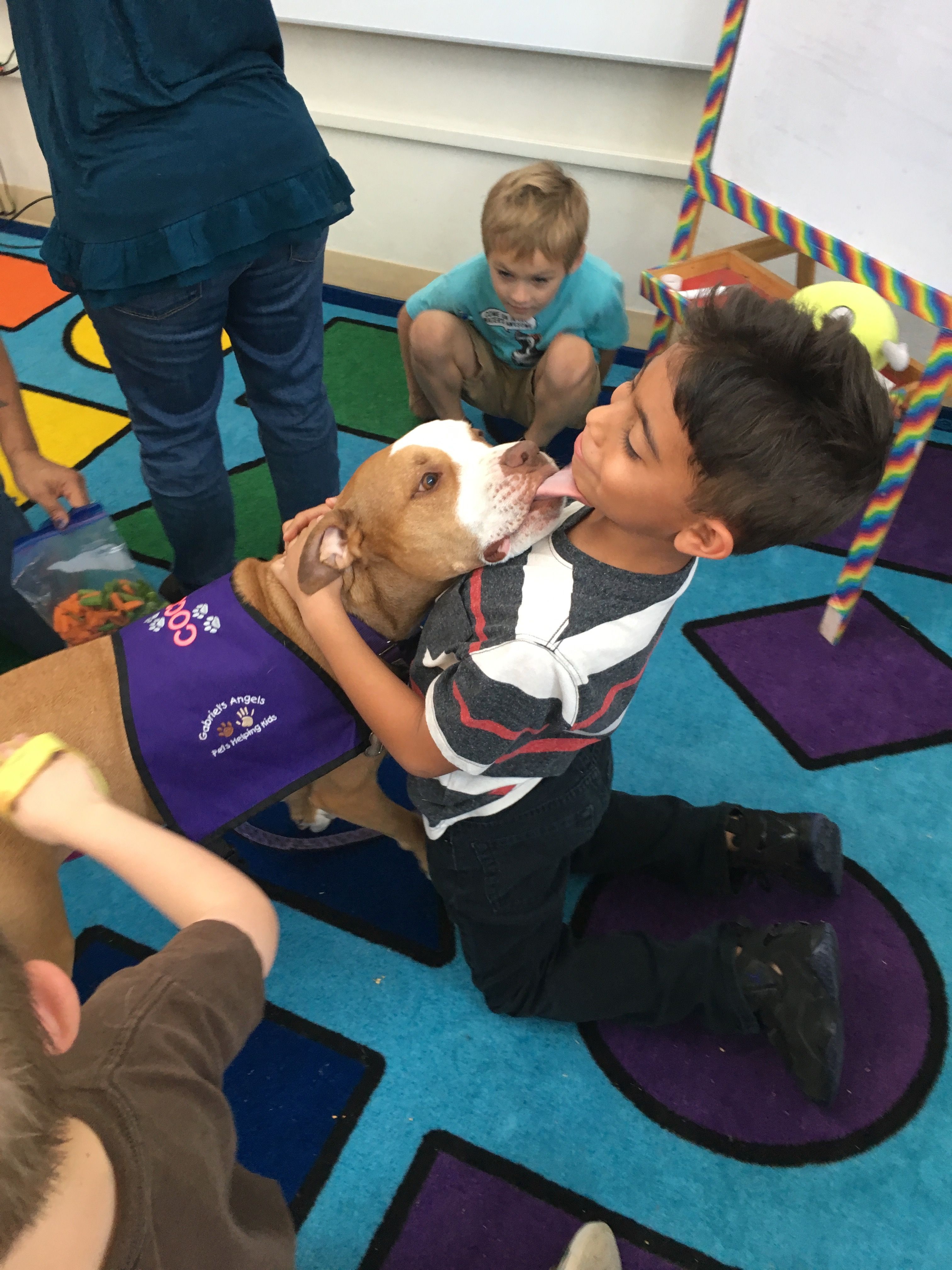 friendly dog surrounded by children, licking one child's face