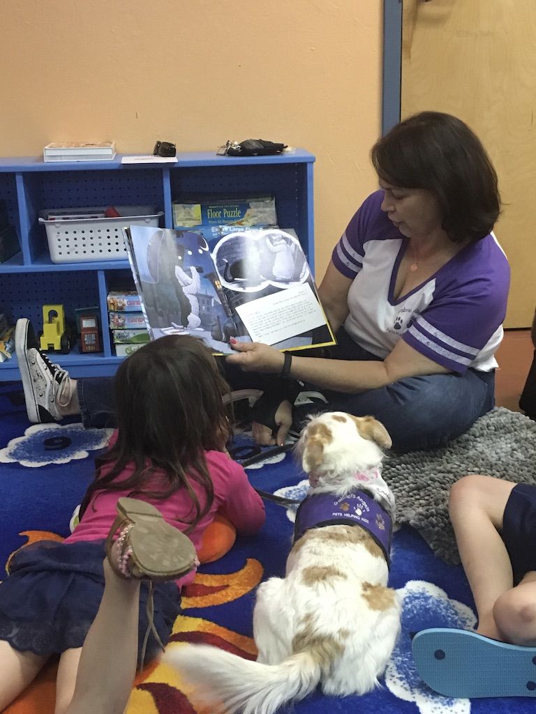 Woman volunteer reading a book to children and therapy dog